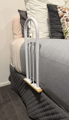 A white arch-shaped bar or lever attached to the upper end of a bed. It is fixed to the bed by a wooden board that extends in between the bed base and the matteress.  